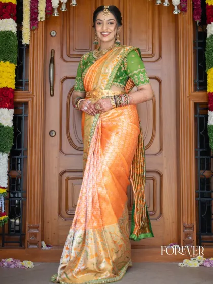 A regal look created by pairing a vibrant orange Kanjivaram saree with a contrasting green embroidered bandhgala blouse. This rich color combination is perfect for a bride who loves to make a statement.