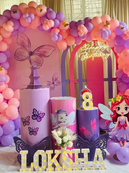 An enchanting fairy and butterfly themed birthday party. This setup uses a pink and purple color scheme with a large balloon arch, themed plinths, and character cutouts.