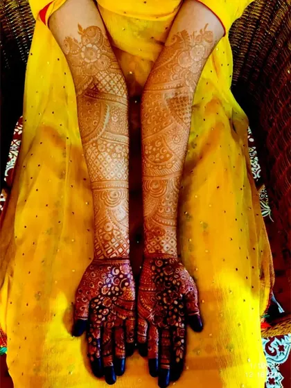 The full bridal look, with henna extending up the arms, complementing the bride's beautiful yellow outfit.