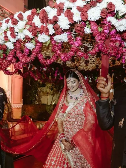 The bride's entry under a beautiful floral 'phoolon ki chadar'. This traditional moment is elevated with a lush arrangement of red and white flowers, making it a truly special part of the ceremony.