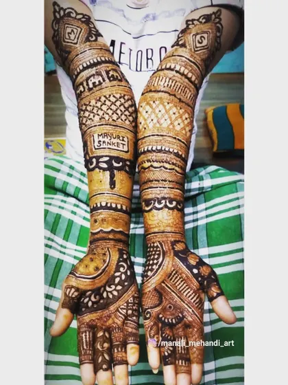 The couple's names, 'Mayuri' and 'Sanket', are integrated into this full-arm bridal mehandi. The design uses bold lines and dense patterns for a striking effect.
