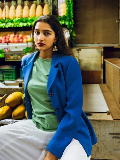 A relaxed pose in a fruit market. The background filled with pineapples and papayas adds a tropical, colorful vibe to this urban fashion shoot.