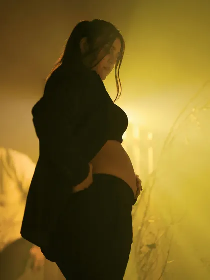 A modern and edgy studio portrait. The mother-to-be is dressed in a stylish black suit, her baby bump visible, creating a powerful and contemporary image of motherhood.