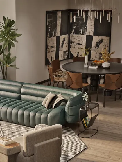 The open layout connects the living room with the round dining table in the background. The green sofa acts as a central piece, while the abstract black and white screen provides a visual separation.