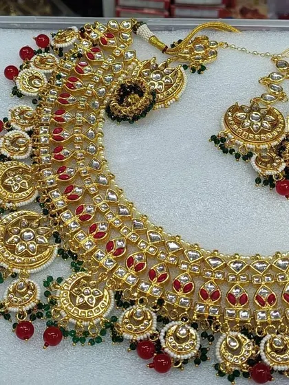 A classic and royal bridal set in red, the traditional wedding color. This jewellery set comes with a detailed choker necklace, matching earrings, and a maang tikka, perfect for a timeless bridal look.