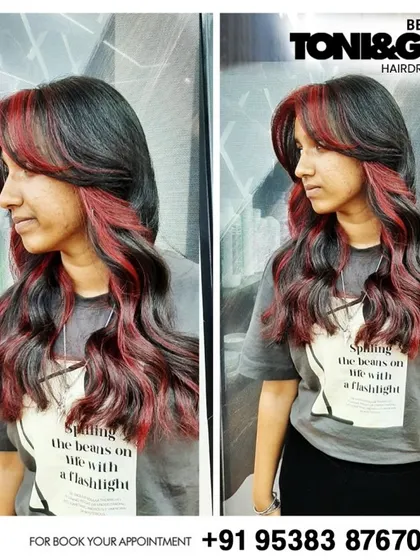 This look features striking red "money piece" highlights at the front. This technique is a great way to add a pop of bold color that frames the face and adds an edge to long, wavy hair.