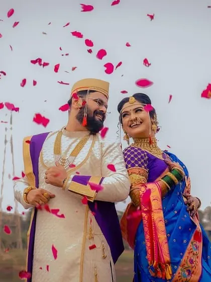 A shower of rose petals rains down on the happy couple. The vibrant colors of their traditional Maharashtrian outfits pop against the sky.