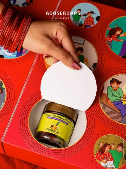 Another surprise revealed. A hand pulls back a perforated circle on the box to show a jar of Assorted Masala Fruit, turning the gift into an interactive experience.