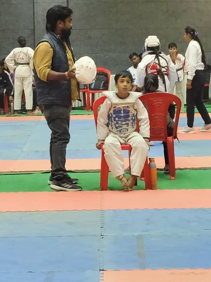 A young Taekwondo player waits for his turn to compete, with his coach by his side. These moments of anticipation are a big part of the competitive experience, teaching patience and focus.