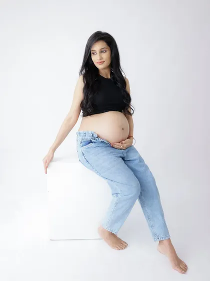 A confident and modern portrait. The mom-to-be rocks a casual look with a black crop top and jeans, showcasing her baby bump with style.