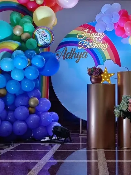 A full view of the rainbow themed stage, including the large light-up number '1' and gold pedestals for the cake and desserts. The bright colors make for fantastic photos.