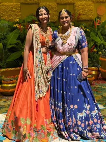 This image shows two of my custom designs together. On the left, an orange silk lehenga with a hand-painted border and Kashmiri work, and on the right, a royal blue lehenga with a unique hand-painted print.