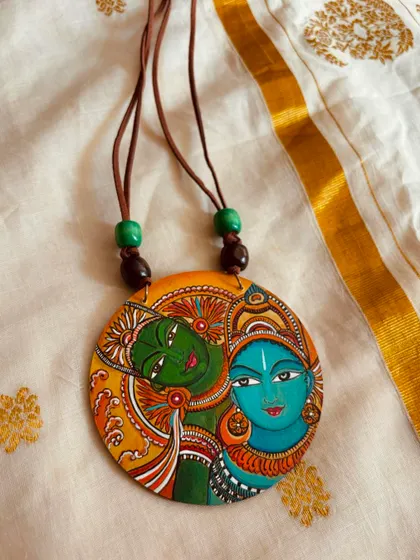 A close-up of my hand-painted Kerala mural pendant, showing the intricate lines and traditional color palette of this beautiful art form.