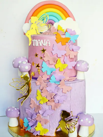 An enchanted wonderland themed two-tier cake. This magical creation features a cascade of butterflies, whimsical mushrooms, and fairy silhouettes.