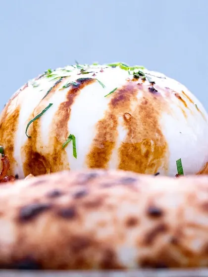 A side-profile of the burrata on the pizza, highlighting its height and the beautiful char marks from the grill. It builds anticipation for the cut.