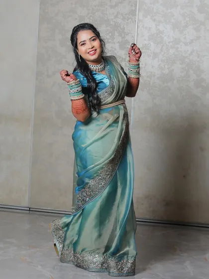 A full-length shot of the bride in a beautiful blue and green saree, captured in a moment of dance and celebration. Her joyful expression and dynamic pose show the fun side of the reception.