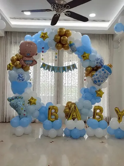 A classic 'Welcome Baby' decoration for a baby boy. This circular balloon arch in blue, white, and gold is filled with fun foil balloons like a baby bottle and footprint, creating a perfect photo spot at home.