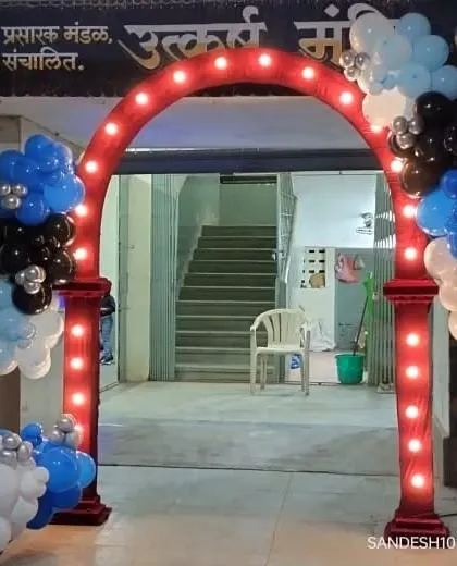 A welcoming entrance arch for a birthday party or event. The red arch is fitted with lights and decorated with garlands of blue, black, and white balloons, creating an exciting entry point for guests.