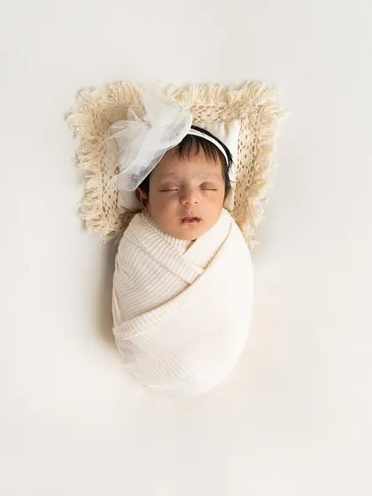 A classic, minimalist portrait. The baby is swaddled in a simple cream wrap against a clean white background, creating a timeless and pure image.