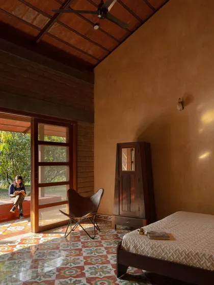 The bedroom is a serene space with exposed earth walls and a large doorway that opens to the outdoors, blurring the boundary between inside and out.