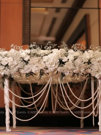 This handcrafted table is a statement piece, featuring a lush arrangement of white flowers and baby's breath draped with elegant strings of pearls. It is perfect as a Nikah signing table, a cake display, or for a ring ceremony.