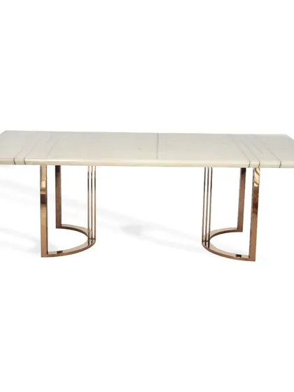 This dining table features a white marble top with linear inlay details. The base is crafted with clean, semi-circular legs in a rose gold PVD finish, creating a cozy and inviting dining space.