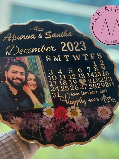 A full view of the custom black resin calendar frame, showcasing the balance between the couple's photo, the calendar details, and the floral arrangement.