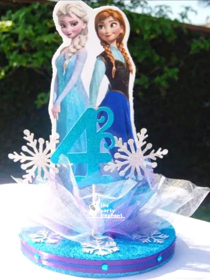 A custom centerpiece for the Frozen party, featuring Elsa and Anna, the birthday number '4', and glittery snowflakes, all tied together with a tulle bow for a magical touch.