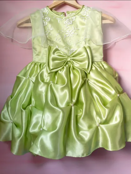 A vibrant lime green satin dress that is sure to stand out. This unique design features a dramatic bubble hem, a large statement bow, and delicate embroidery on the bodice for a fun and high-fashion look.