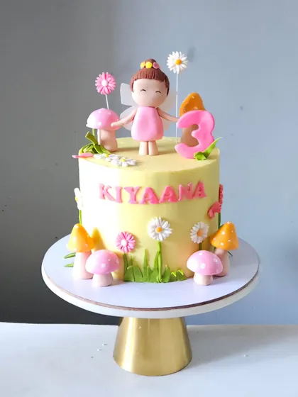Welcome to fairyland with this sweet and simple cake for a third birthday. It's decorated with a cute fairy topper, edible pink and orange mushrooms, and little flowers to create a magical garden scene.