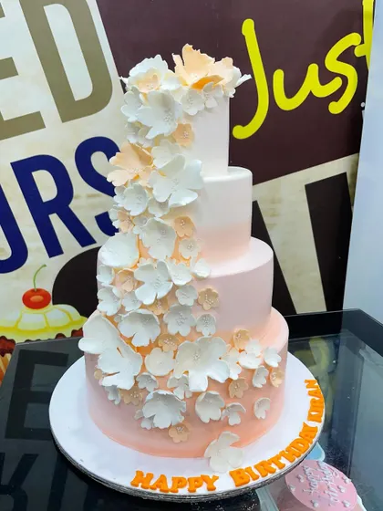 A sophisticated 7kg three-tiered cake with a soft pink ombre effect, featuring a cascade of handmade white and peach sugar flowers.