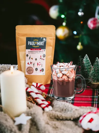 A cozy scene with a mug of hot chocolate topped with marshmallows, a pack of Christmas spice mix, and a lit candle, evoking warmth and comfort.