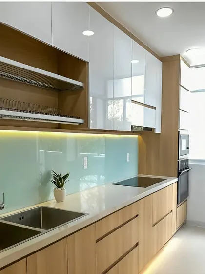 A minimalist kitchen design featuring handleless wood cabinets and a calming light blue glass backsplash. The under-cabinet lighting provides excellent task illumination while adding to the clean and modern aesthetic.