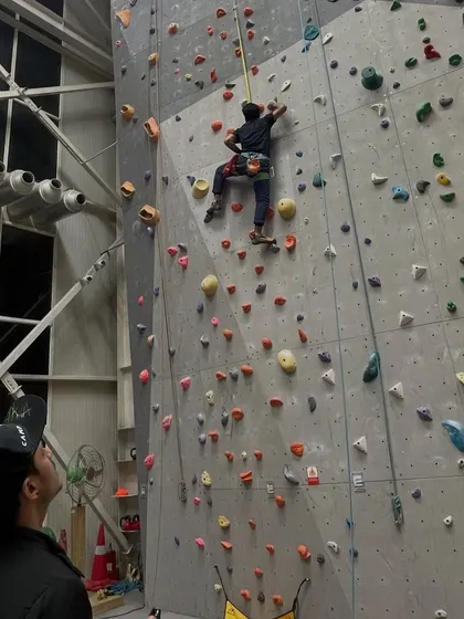 A belayer watches his partner ascend one of our tall indoor walls. The scale of our gym means there are always new heights to conquer.