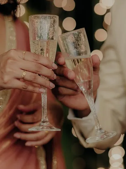 A close-up of the couple's hands as they clink their champagne glasses.