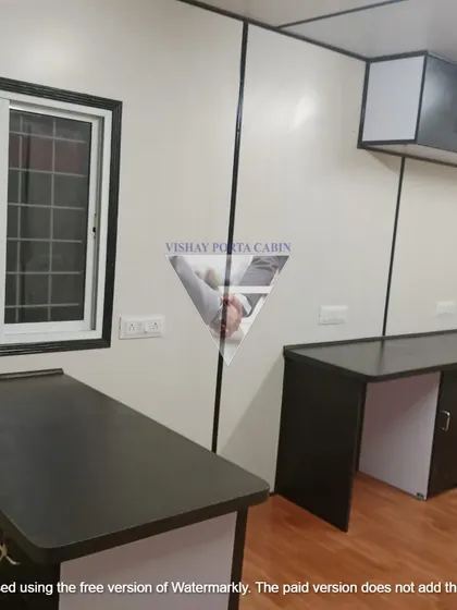 This image highlights a practical office interior with multiple desks and overhead storage. You can see the clean wall panels, durable flooring, and a sliding window with a security grill, making it a secure and functional workspace.