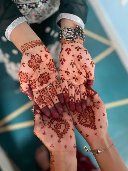 A closer look at two different party henna styles. One is a simple heart design, and the other is a more traditional floral pattern.