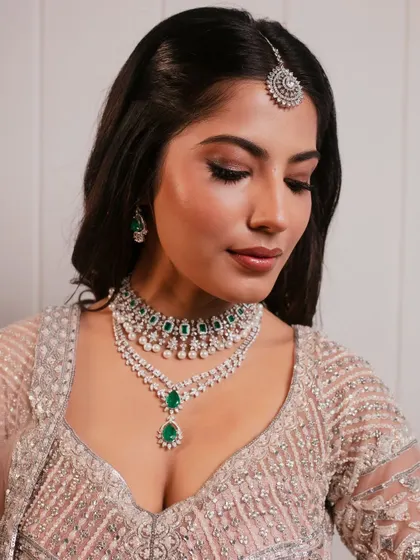 A modern bridal look with a soft pink lehenga and striking emerald jewelry, complemented by a subtle smokey eye.