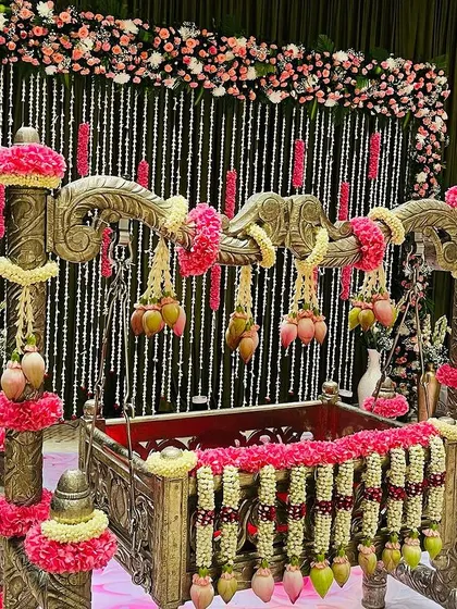 An elegant naming ceremony setup with a beautifully decorated cradle. The backdrop features hanging strings of jasmine and pink floral accents, creating a delicate and charming atmosphere.
