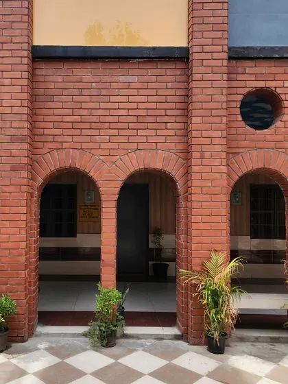 A close-up of the brick columns and arches, showcasing the material's texture and the simple geometry used throughout the facade renovation. Potted plants add a touch of green to the warm brick tones.