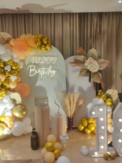 A boho-glam 18th birthday setup. This design combines a neutral color palette and pampas grass with the sparkle of gold balloons and marquee numbers.