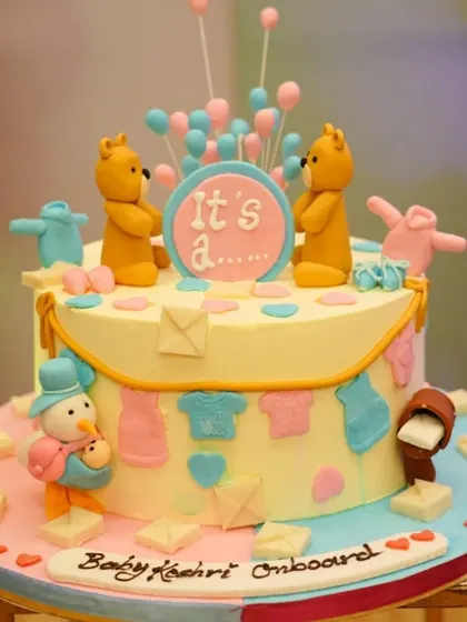 "It's a..." This gender reveal cake is full of suspense and sweetness! Decorated with teddy bears and a clothesline of baby outfits in pink and blue, it's a fun centerpiece for the big reveal.