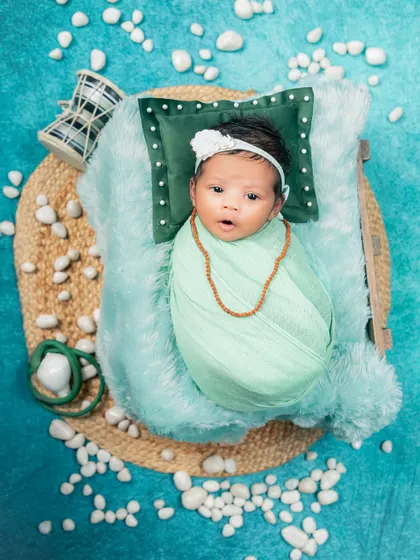 An overhead shot of the Maha Shivratri theme, providing a full view of the creative setup. The baby is swaddled and lies on a jute mat surrounded by white pebbles, a damru, and a soft pillow.
