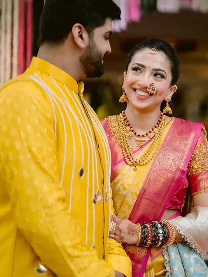 The way a bride looks at her partner is pure magic. Here, her radiant smile is the centerpiece, enhanced by a makeup look that is both traditional and fresh. The bright yellow and pink saree adds to the festive wedding atmosphere.