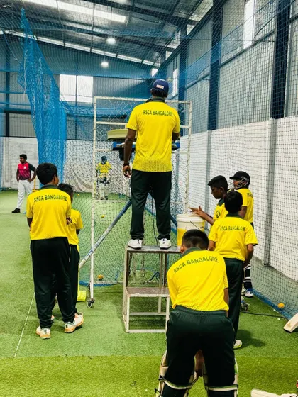 A coach provides one-on-one guidance from an elevated platform during an indoor net session, a technique we use for better analysis of a player's form.