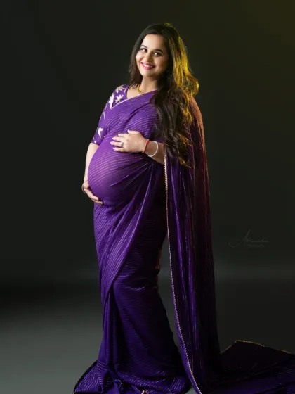 A beautiful solo portrait showing the baby bump. The side lighting highlights her form, and the purple saree adds a pop of vibrant color.
