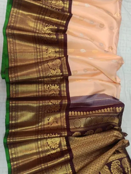 A beautiful pure Gadwal silk handloom saree in a pastel peach color with a rich, dark traditional border.
