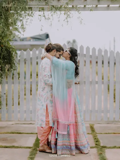 A romantic embrace in front of a white picket fence, a quiet moment amidst the fun celebration.