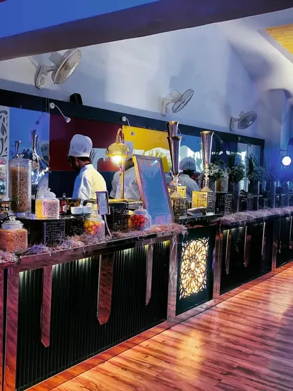 This rustic buffet setup features wooden counters and a variety of snacks displayed in large glass jars. The warm, moody lighting is perfect for an evening sangeet or reception.