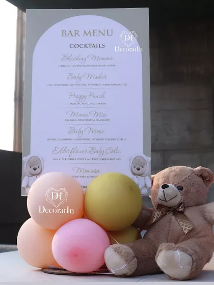 A custom bar menu for a baby shower, displayed with a teddy bear and balloons.